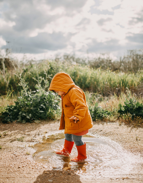 baby wearing a rain jacket is playing in a small puddle of water
