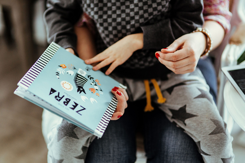 toddler reading little book sitting on his mom's lap