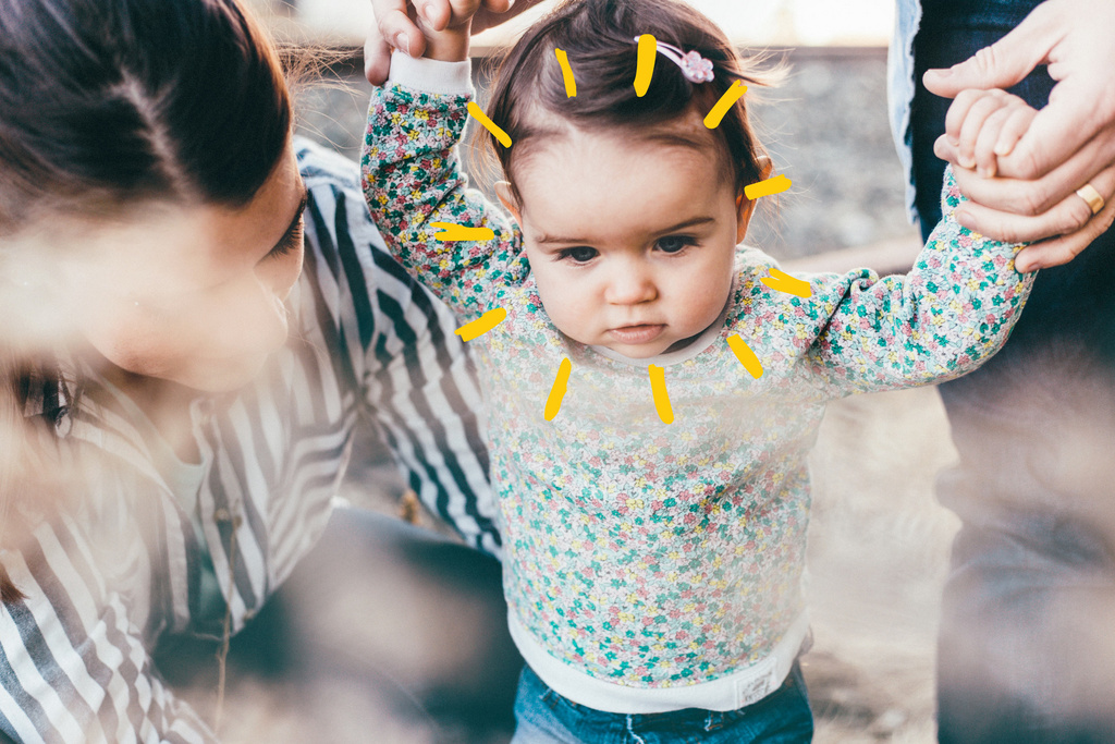 dad holding babys hands and mother tying lays sunshine 